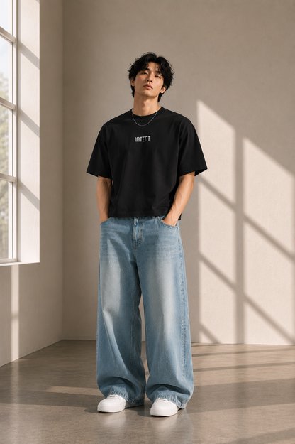 Person wearing Intent's black bamboo oversize t-shirt and blue jeans standing in a sunlit room.